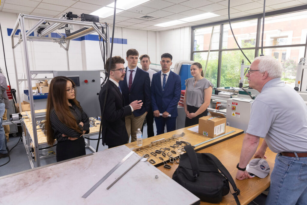 Photo of UW-Stout seniors discussing their capstone project on behalf of Cirrus Aircraft. The automated system behind them was designed to chemically coat machined aircraft parts.