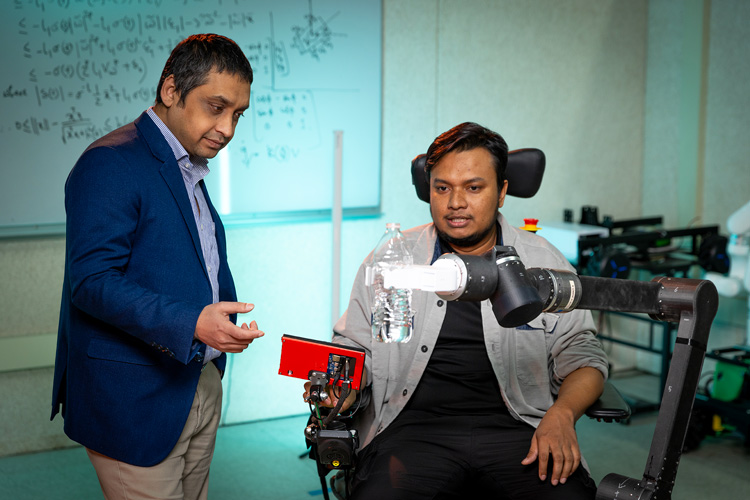 Photo: Habib Rahman (left), director of UWM's Biorobotics Lab, and PhD student Md Mahafuzur Rahaman Khan demonstrate their lab's assistive robotic arm that could be mounted to wheelchairs to help stroke and spinal cord injury patients perform everyday tasks. (UWM Photo/Troye Fox)