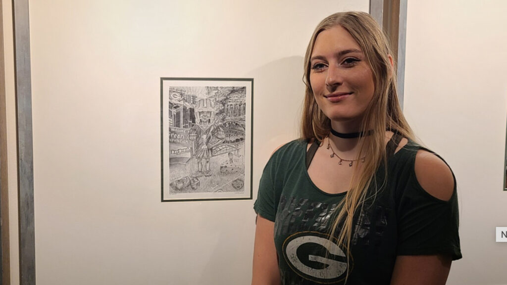 Photo of UW-Platteville alumna Trinity Schlorf with her piece of art hanging at Lambeau Field