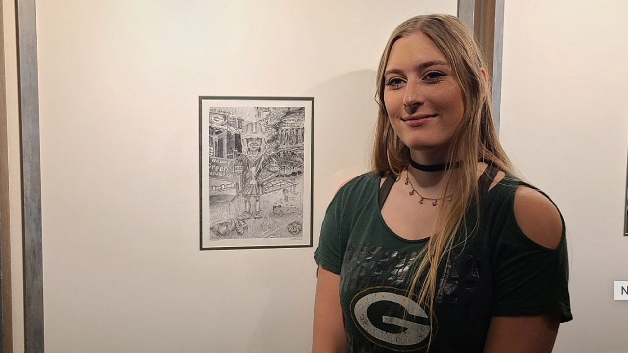 Photo of UW-Platteville alumna Trinity Schlorf with her piece of art hanging at Lambeau Field