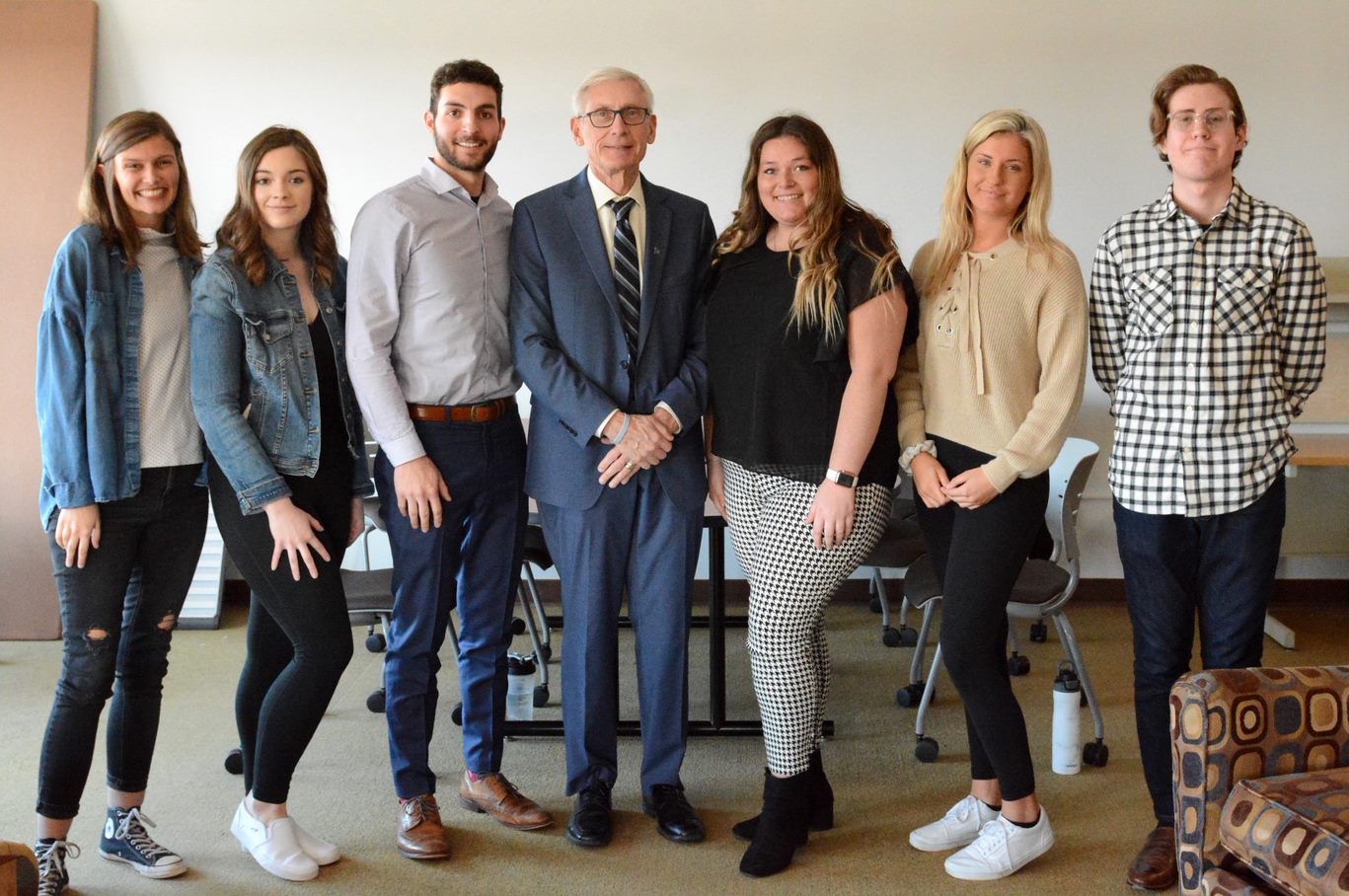 Governor Tony Evers stands casually in the center of a group of six college students. 